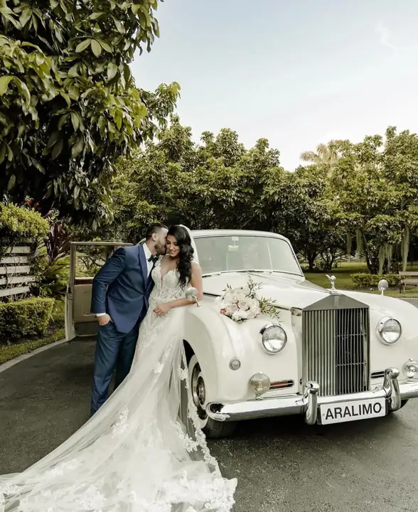 Couple posing beside vintage wedding car